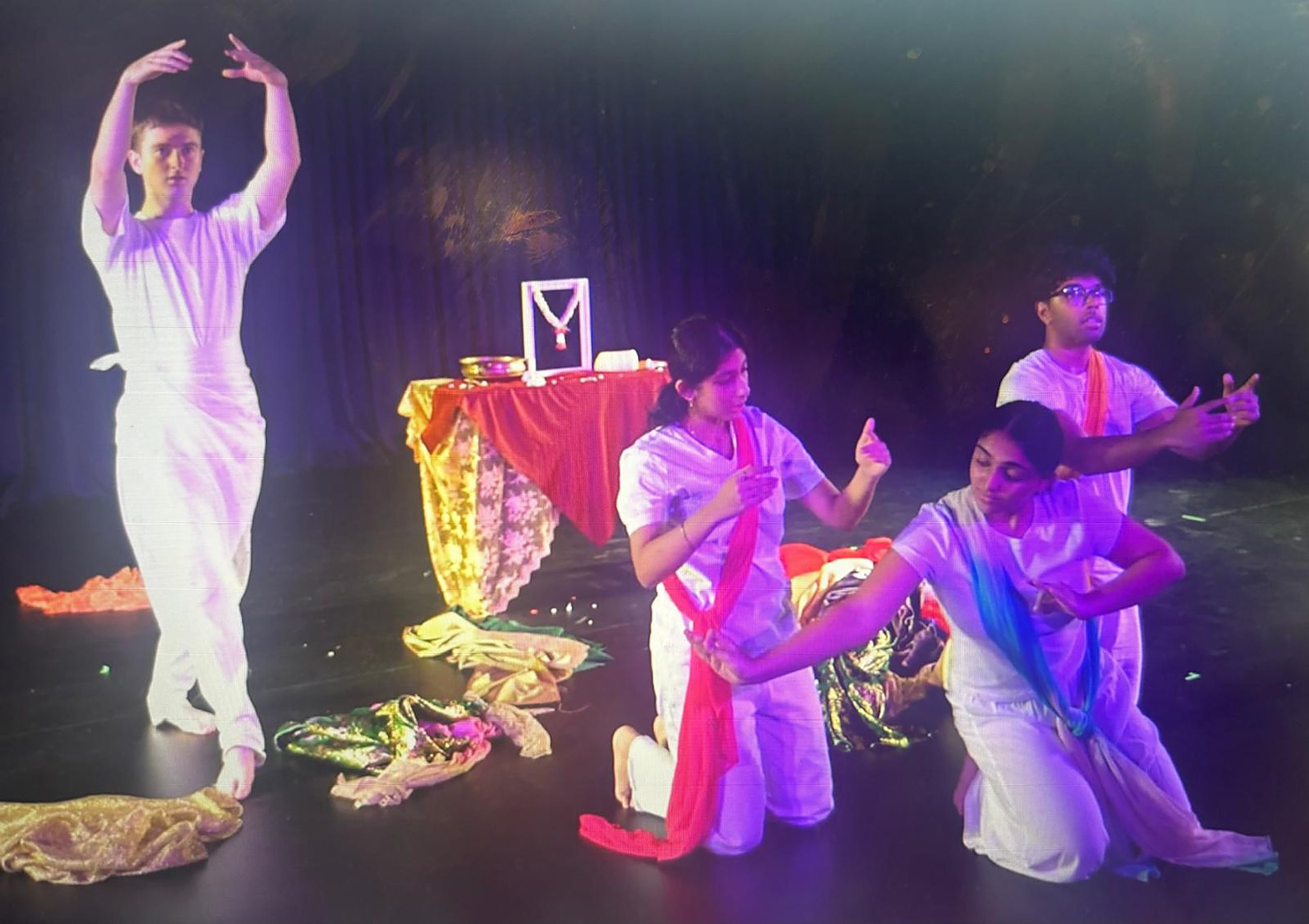 Andrei, arms raised, leads an ensemble in white among coloured fabric