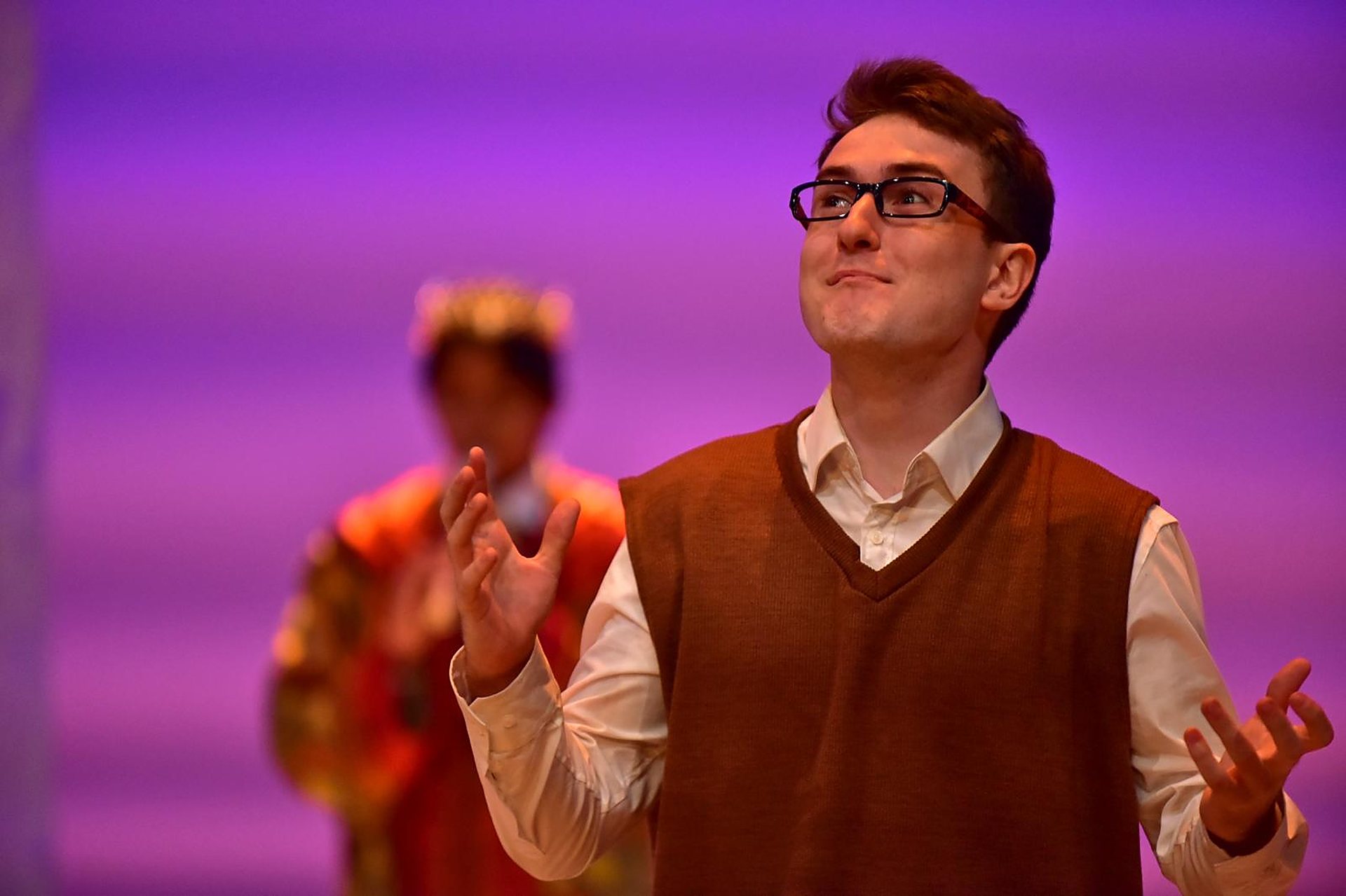 Andrei mid-gesture, eyes up, in a sweater vest under violet light