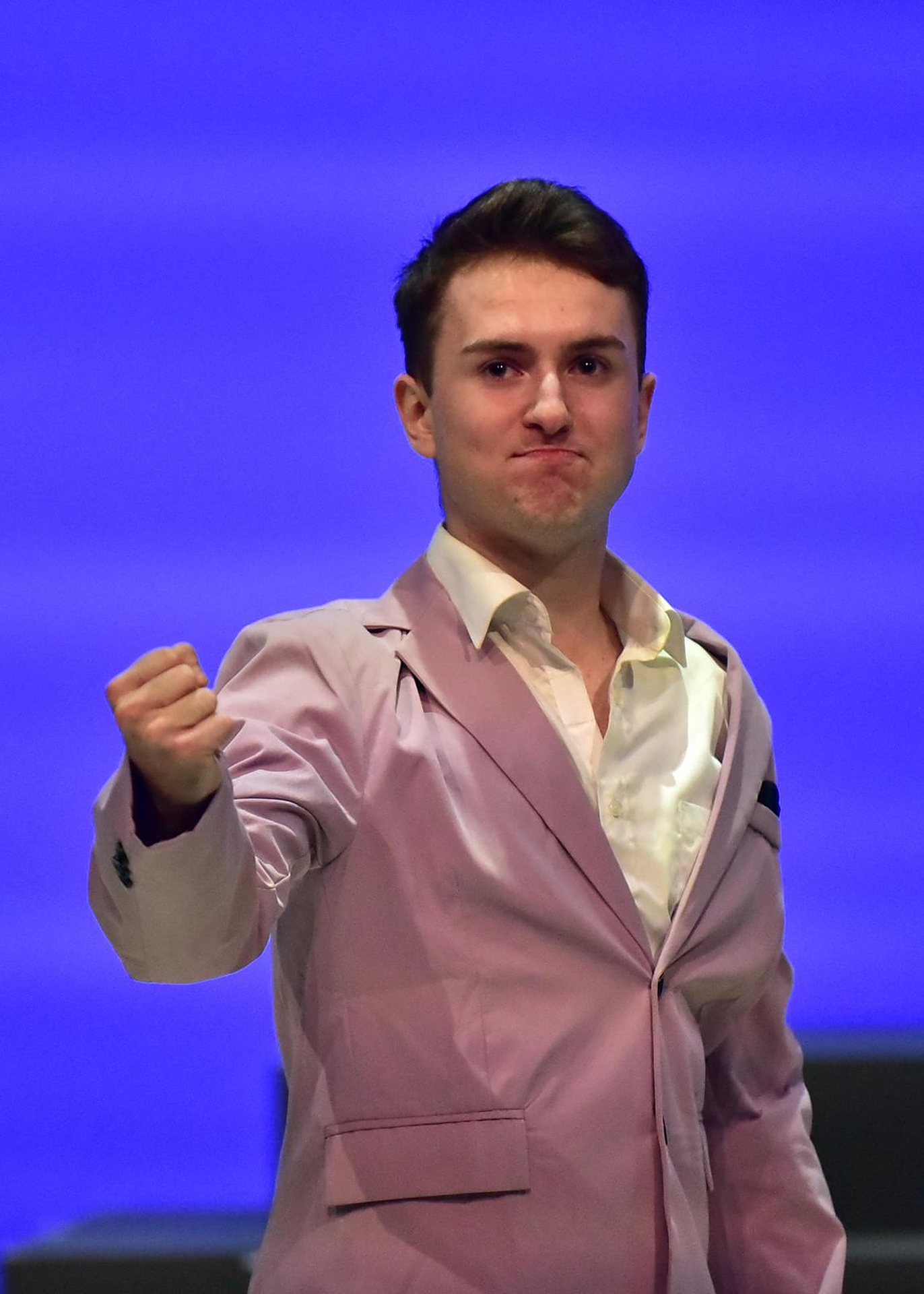 Andrei in a pale suit, fist clenched, against blue light